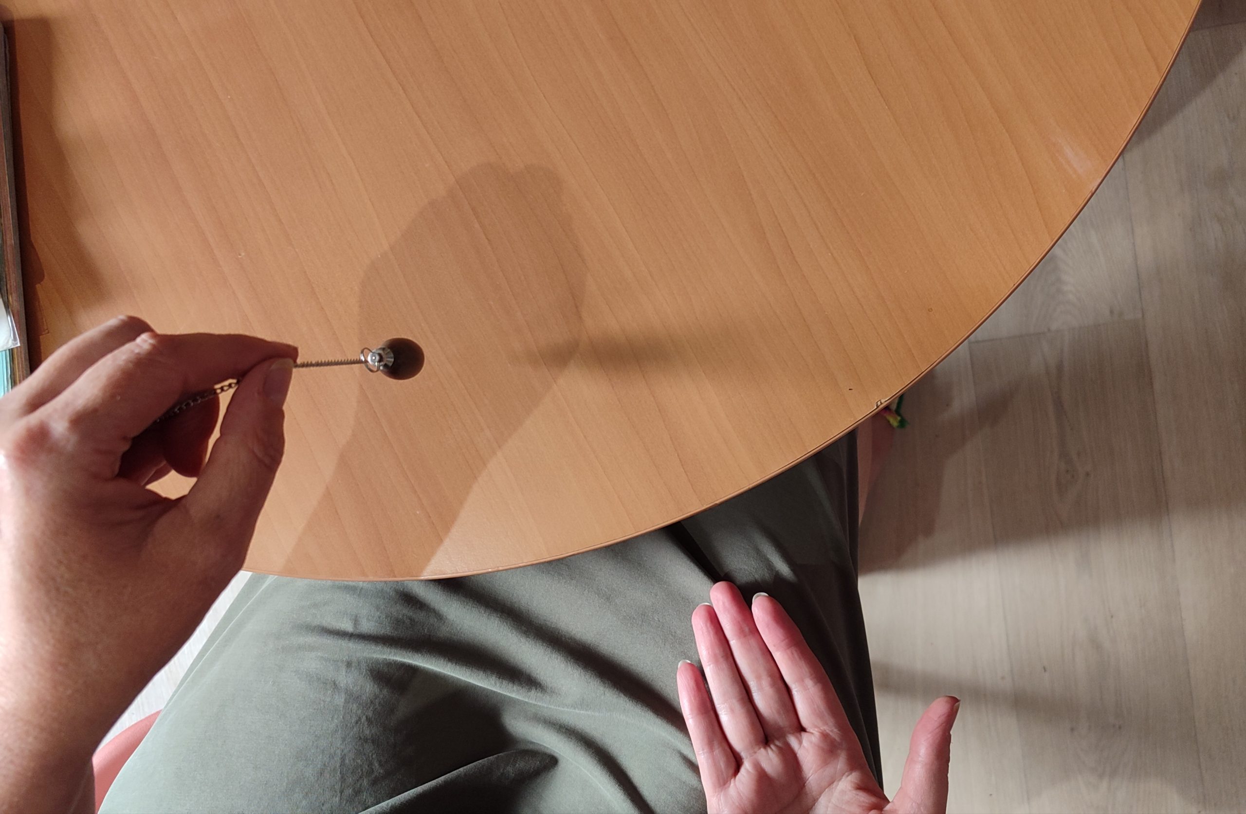 Utilisation du pendule pendant une séance de soin énergétique, au-dessus des planches de radiesthésie